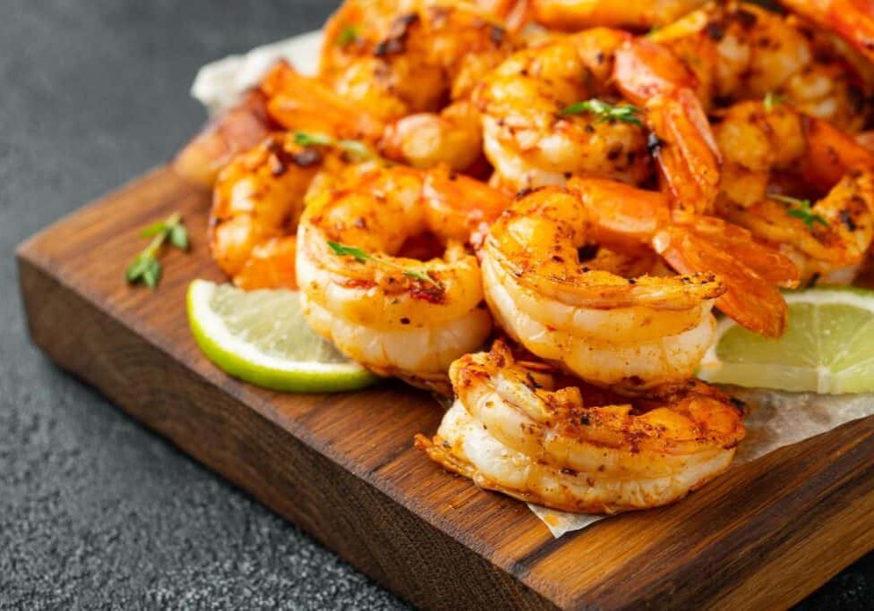 Grilled shrimps or prawns served with lime, garlic and white sauce on a dark concrete background. Seafood.